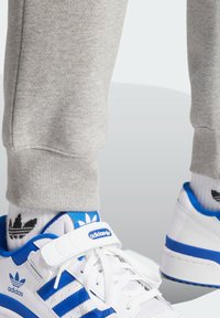 Pelēki kokvilnas sporta bikses ar ribotām piedurknēm, apvienotas ar baltām kedām ar zilām akcentiem un trīs slīpēm.