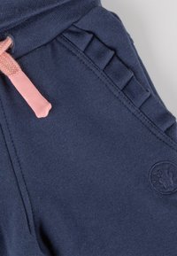 Marineblaue Jogginghose aus weichem Material, mit einem gerippten Bund, pinkem Kordelzug und Rüschendetails an den Seiten.