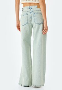 Ljust tvättade jeans med vida ben och hög midja, med två bakfickor och synlig sömnad. Materialet har en mjuk textur.