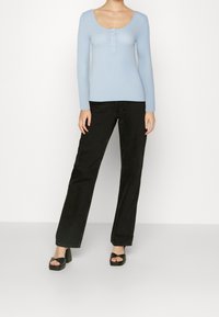 Light blue ribbed long-sleeve top with a scoop neckline and three-button placket, paired with high-waisted black straight-leg jeans and black sandals.