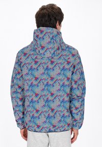 Giacca a vento colorata con cappuccio, caratterizzata da un motivo geometrico in blu, rosso e rosa. Realizzata con un tessuto testurizzato, maniche elastiche e orlo.