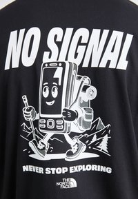 T-shirt noir avec un graphique blanc représentant un téléphone mobile cartoon portant un sac à dos, en train de faire une randonnée dans un paysage montagneux, avec du texte au-dessus et en dessous.