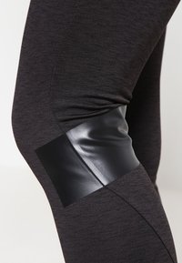 Leggings neri con una combinazione di tessuti morbidi e accenti lucidi neri sulle ginocchia. Il design presenta una silhouette aderente.