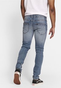 Jeans de mezclilla azul de corte slim, con bolsillos traseros, un ligero desvanecido y detalles de costura. Combinados con zapatillas negras y blancas.