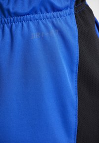 Närbild av blå sporttyg med elastisk midja och svart meshpanel, som har svag "DRI-FIT" text.