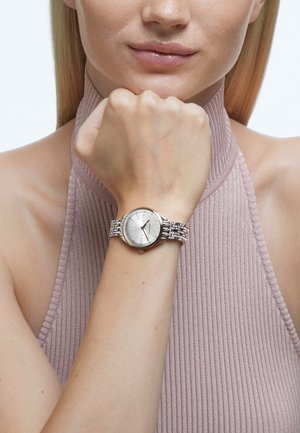 Silver watch with a round face, textured silver dial, crystal accents on a metallic bracelet, worn on a light-skinned wrist.