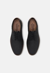 Chaussures noires à lacets avec une surface texturée, accents marron et semelle cousue. L'intérieur comprend une semelle intérieure rembourrée et estampillée.