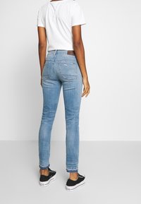 Jeans ajustados de un azul claro con acabado desgastado, que cuentan con una cintura de altura media, bolsillos traseros y detalles de costura. Combinados con deportivas negras.