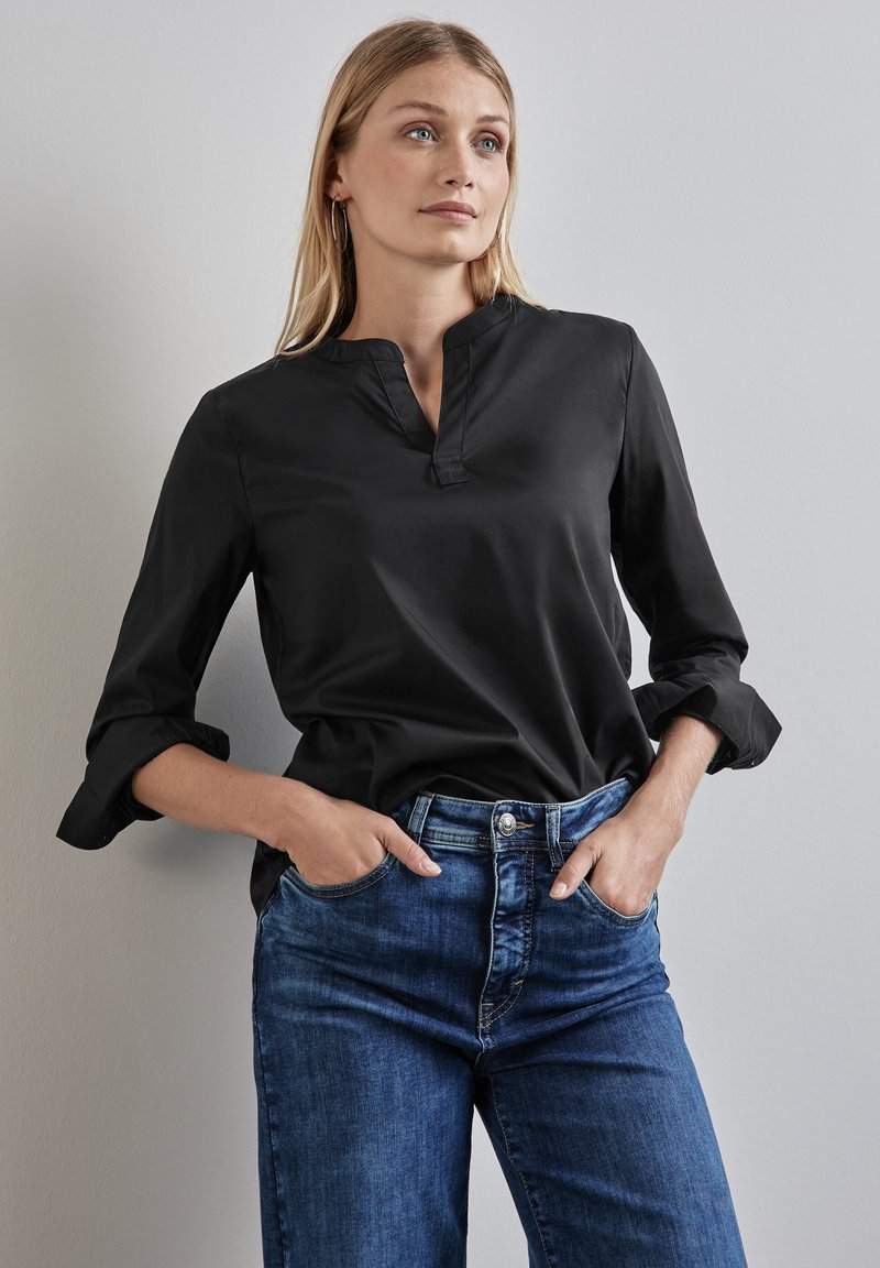 Camicia nera a maniche lunghe con colletto stand-up, realizzata in tessuto liscio. Abbinata a jeans in denim blu medio con vestibilità classica e cinque tasche.
