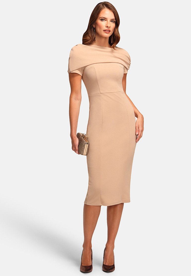Aansluitend beige jurk met korte mouwen en gedrapeerde buste, die onder de knie reikt. Gecombineerd met een metalen clutch en bruine hakken.