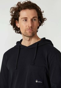 Sudadera azul marino, de material de algodón, con un bolsillo frontal, capucha con cordón y un pequeño logotipo en el bolsillo. Textura suave.