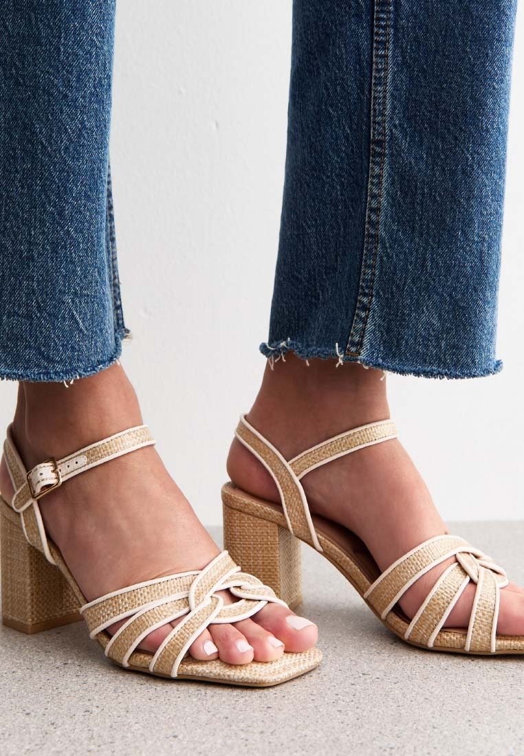 Sandales à talons hauts beiges à brides, avec un design tissé texturé, bout carré et talon épais, portées avec un jean en denim à ourlet effiloché.