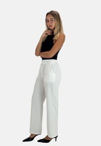 Hvide bukser med vide ben og glat tekstur, der har sidelommer og lynlås. Kombineret med sorte spidse hæle og en sort top.