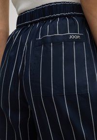 Pantaloni blu navy con strisce bianche verticali, dotati di una cintura elastica e una tasca posteriore con il logo "JOOP!" ricamato.