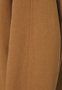 Tela de punto marrón con una textura suave. Presenta costuras visibles y un patrón uniforme. Apariencia ligeramente cepillada.