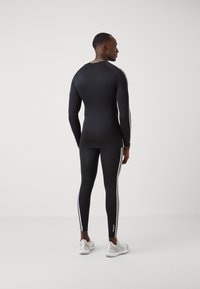 Fekete sportos bodysuit hosszú ujjal és kontrasztos fehér csíkokkal az oldalakon. Illeszkedő fazonnal és sima textúrával tervezték.