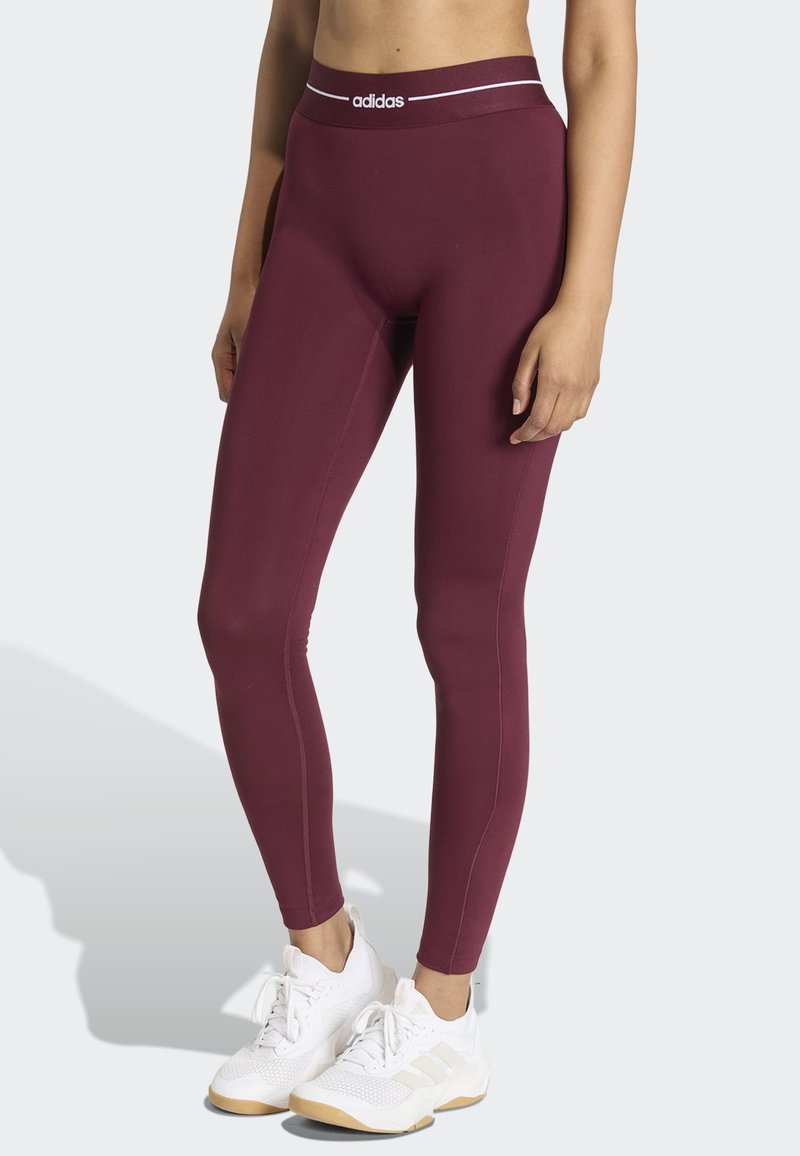 Leggings color granate con una cinturilla alta que presenta un logo blanco de adidas. La tela es suave y elástica, diseñada para ropa deportiva.