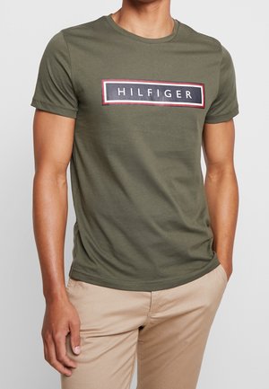 oliwkowy t-shirt bawełniany z krótkim rękawem z czarnym i czerwonym prostokątnym logo "HILFIGER" na piersi.