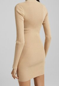 Abito a maniche lunghe in maglia di colore beige, design aderente, texture morbida e orlo fino al ginocchio. Dettagli delle cuciture lungo la schiena e le maniche.