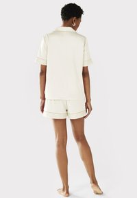 Ensemble de pyjama crème à manches courtes avec un col, mettant en valeur des bords sur les manches et le short. Matière douce, coupe décontractée, short avec une taille élastique.