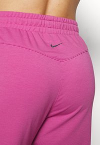 Zbliżenie osoby noszącej jaskrawo różowe legginsy Nike z elastycznym pasem i czarnym logo Nike na tyle.