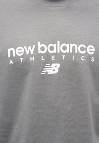 Γκρι αθλητικό μπλουζάκι από βαμβακερό μείγμα ύφασμα με έντονο λευκό κείμενο "new balance ATHLETICS" και λογότυπο στο στήθος.