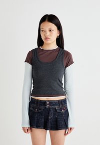 Gray ribbed tank top layered over a brown short-sleeve shirt, paired with a dark denim pleated skirt featuring two buttons and pockets.
