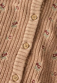 Megzta švarko tipo megztinė švelnios smėlio spalvos su gofruota tekstūra, puošta gėlių siuvinėjimu bordo ir žalia spalvomis, su mediniais sagomis.