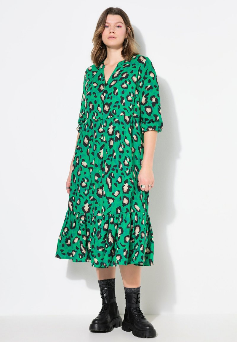 Abito verde con motivo animalier a macchie di leopardo, gonna a strati, scollatura a V, maniche a tre quarti, abbinato a stivaletti neri chunky.