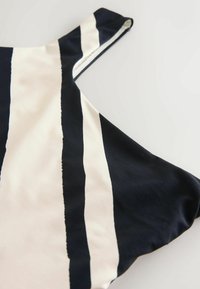 Beži naudoti viršūnė su ryškiomis tamsiai mėlynomis ir kreminėmis juostomis. Audinys yra lygus, su apvaliu iškirpimu ir laisvu siluetu.