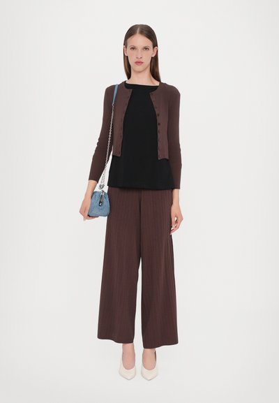 Brun ribbet cardigan over en svart topp, kombinert med brune plisserte vide bukser. Kremfargede spisse hæler og en blå veske.
