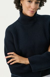 Navy ribbed turtleneck sweater with long sleeves and relaxed fit. Features textured knit pattern and wide cuffs for added detail.