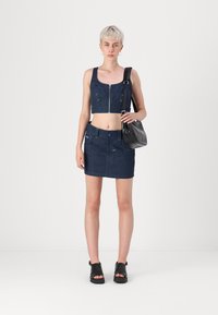 Denim prirezana majica s prednjim zipperjem in naramnicami, kombinirana z visokim denim krilom. Črna torbica in sandali dopolnjujejo videz.