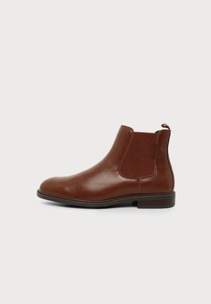 Brauner Leder-Chelsea-Stiefel mit elastischem Seitenpaneel und Zuglasche, niedrigem gestapeltem Absatz und rund zulaufender Spitze auf weißem Hintergrund.