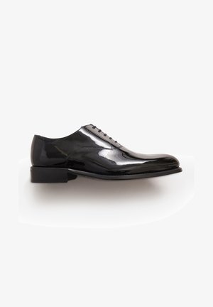 Scarpa nera da uomo con finitura in vernice lucida e liscia. Presenta sei occhietti per i lacci e un tacco basso impilato. Forma classica della punta arrotondata.