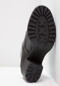 Bota de cuero negra con una suela de goma texturizada que presenta un diseño de tacos. Los acentos notables incluyen una costura y un logo de la marca embosado.