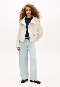 Κοντό διπλόχτονο κρεμ σακάκι με μεγάλα κουμπιά, συνδυασμένο με μπλε ναυτικό τοπ και φαρδιά ανοιχτή τζιν παντελόνια. Μαύρα επίπεδα παπούτσια.