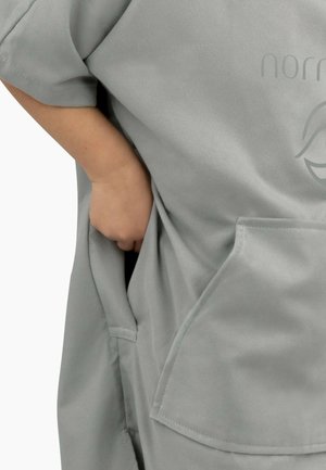 Graues, übergroßes Kleidungsstück mit kurzen Ärmeln, aus weichem Material gefertigt, mit großen Fronttaschen und einem dezenten Logo auf dem Stoff.