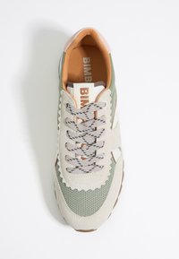 Lichtbeige sneaker met olijfgroene accenten, gestructureerd suède, gaaspanelen en bedrukte veters. Voorzien van een roze hiel en logo op de tong.