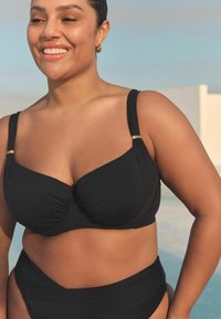Schwarzer Bikini-Oberteil mit strukturiertem Design und gerafftem Stoff, mit breiten Trägern mit goldenen Akzenten, kombiniert mit hochtaillierten Slips.