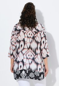 Loose-fitting blouse made of lightweight fabric in white, black, and coral with geometric patterns, three-quarter sleeves, and a curved hem.