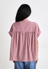 Ροζ ριγέ μπλούζα με κοντά μανίκια, με μαζεμένο σχέδιο στην πλάτη και μικρή κουμπί στο λαιμό. Ελαφρύ ύφασμα.