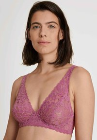 Bralette in pizzo color mauve con design a V. Presenta motivi floreali, bordi scallop e spalline regolabili. Texture morbida e trasparente.