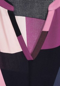 Vícebarevný top s výstřihem do V, s částmi v růžové, fialové, tmavě hnědé a černé barvě, vyrobený z měkké látky s hladkým povrchem.