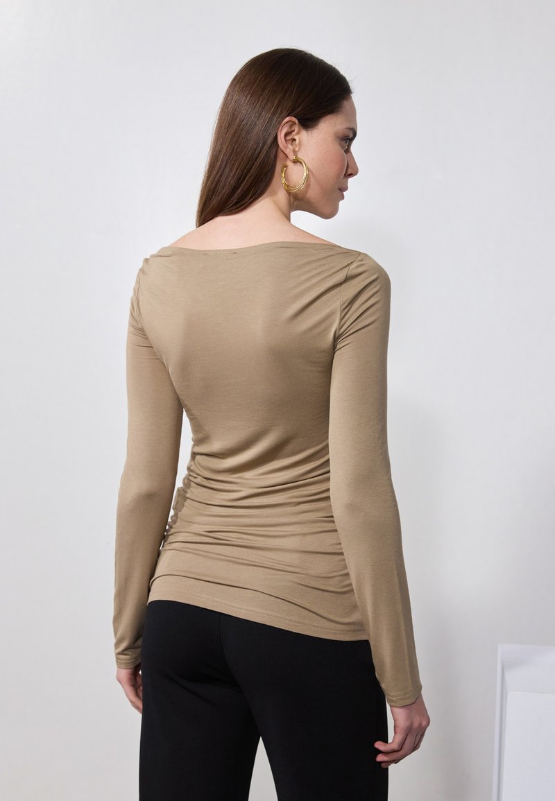 Długi rękaw w jasnobrązowym kolorze, z okrągłym dekoltem i marszczonymi bokami, wykonany z miękkiego materiału, który dopasowuje się do sylwetki.