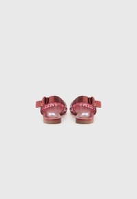Sandales rouges avec une sangle texturée et un talon élastique, design ouvert à l'avant et semelle plate. Présente un motif découpé décoratif sur les côtés.