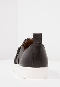 Baskets en cuir noir à texture lisse, dotées d'une semelle en caoutchouc blanche et d'une languette arrière relevée pour un enfilage facile.