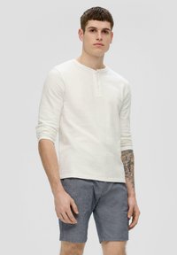 Weißes Langarm-Henley-Shirt mit einer Drei-Knopf-Leiste und hochgerollten Ärmeln, kombiniert mit grauen Shorts. Glatte Textur, lässige Passform.