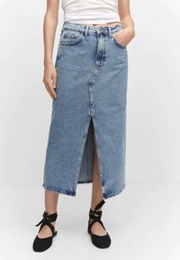 Denim-maksihame, jossa on etuhalkio, vaalea sininen pesu, viisi taskua, ommeltu yksityiskohta ja raakapää, yhdistettynä mustiin nauhakengiin.