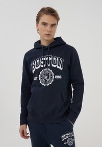 Felpa navy con tasca frontale, caratterizzata da un testo bianco "BOSTON" e un emblema circolare. Realizzata in un morbido misto cotone, con cappuccio regolabile.